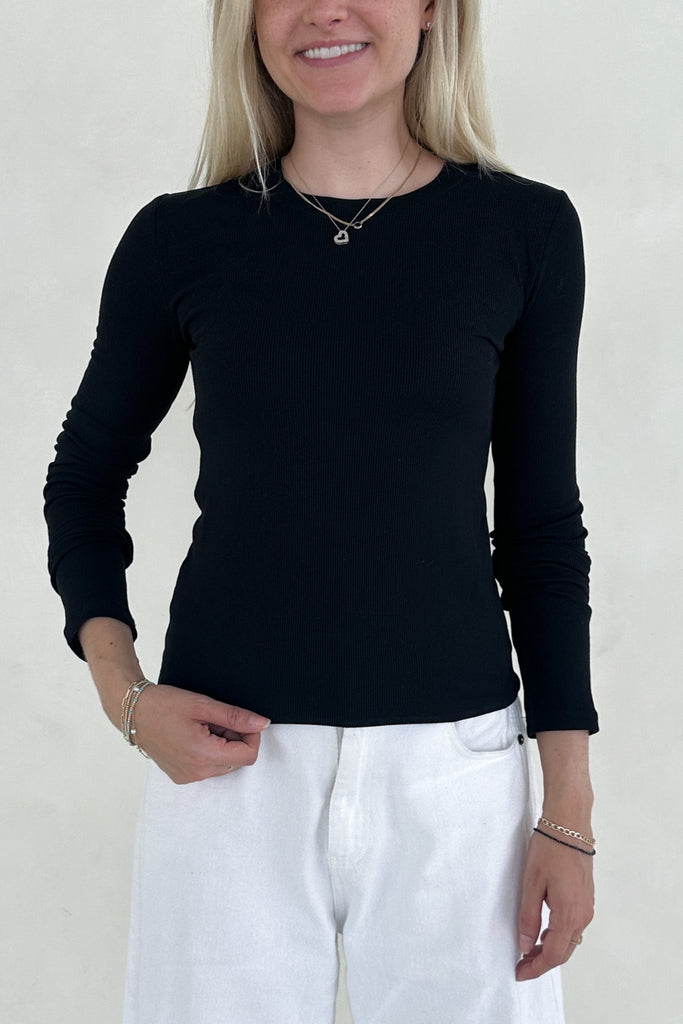 Person wearing a black long-sleeve top and white pants against a plain background