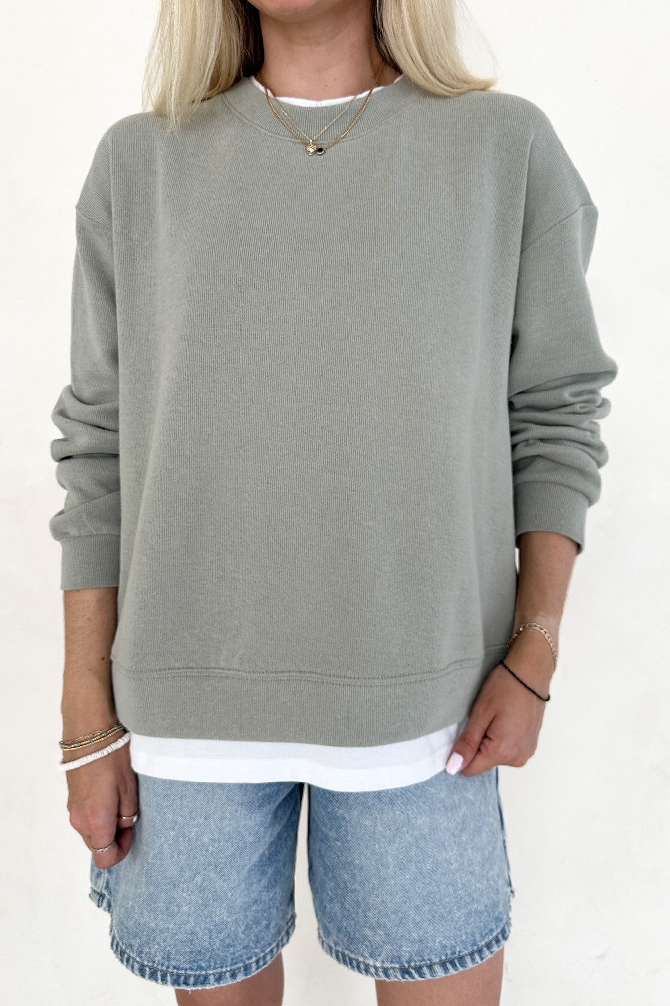 Person wearing a green sweatshirt and denim shorts on a white background