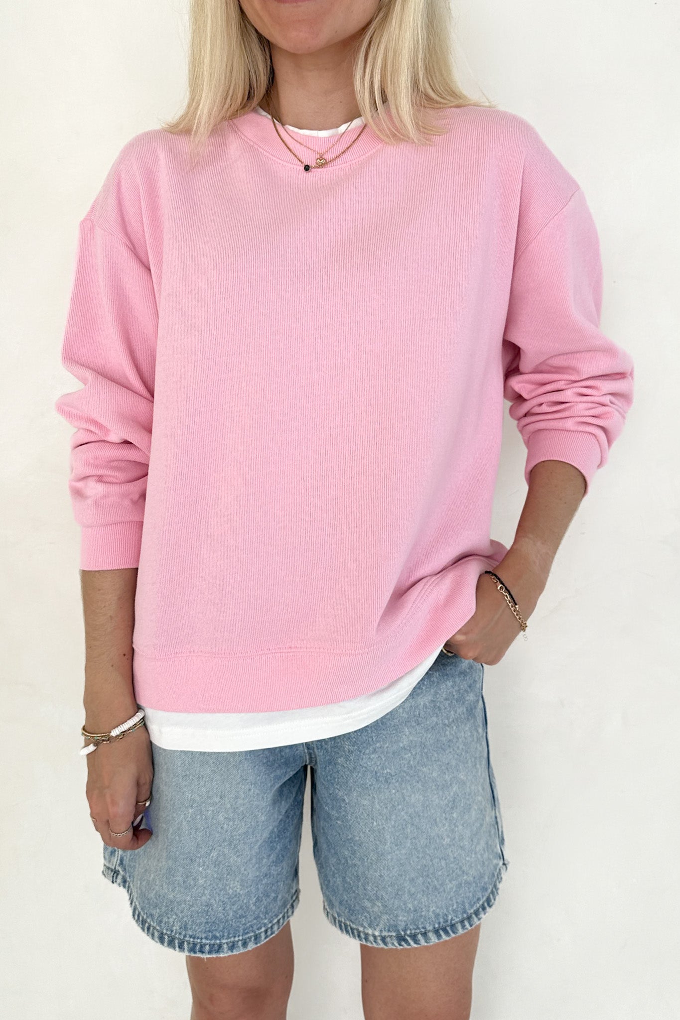 Person wearing a pink sweatshirt and denim shorts on a white background