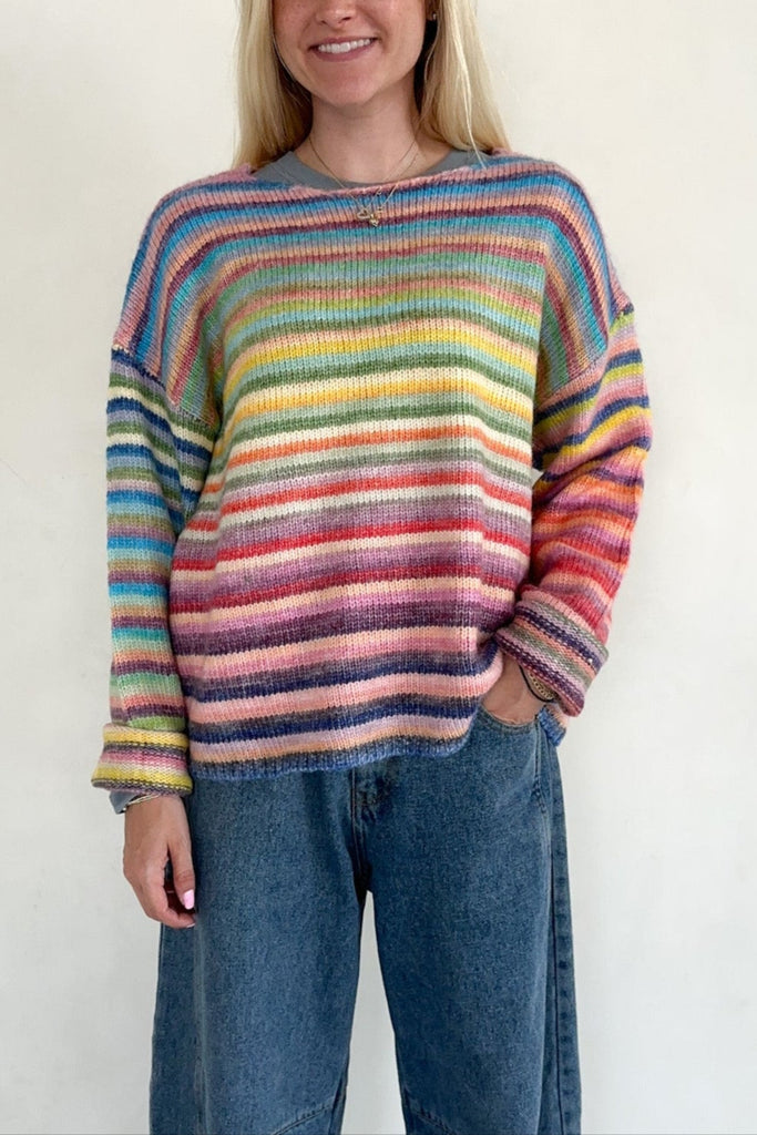 Person wearing a colorful striped sweater and jeans on a white background