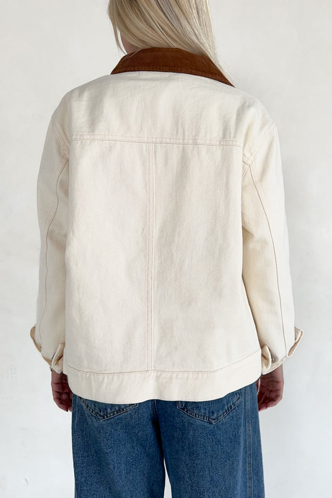 Person wearing a cream denim jacket with a brown collar on a white background