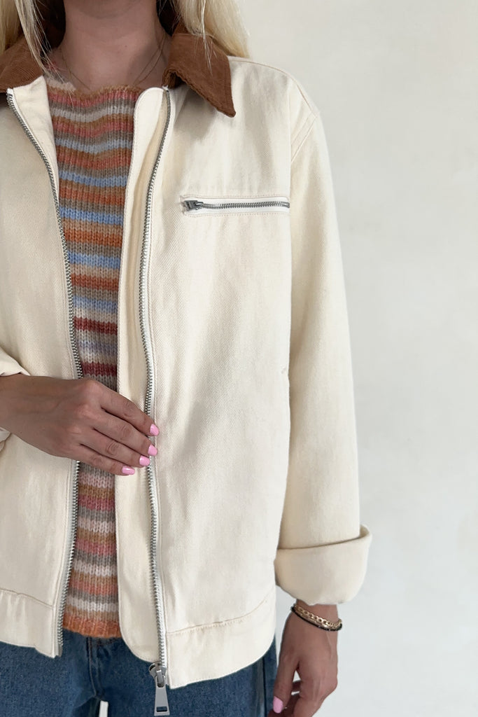 Person wearing a beige jacket with a striped sweater underneath on a white background