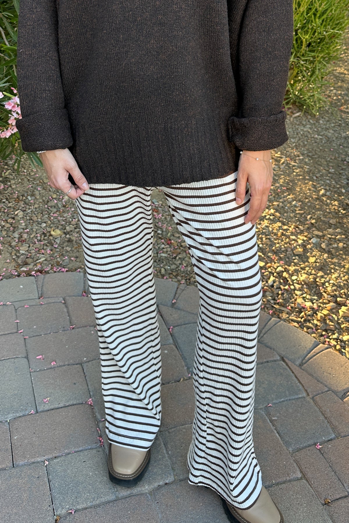 A person wearing black and white horizontally striped wide-leg knit pants, paired with a dark brown knit sweater and tan shoes, standing on a paved outdoor walkway.