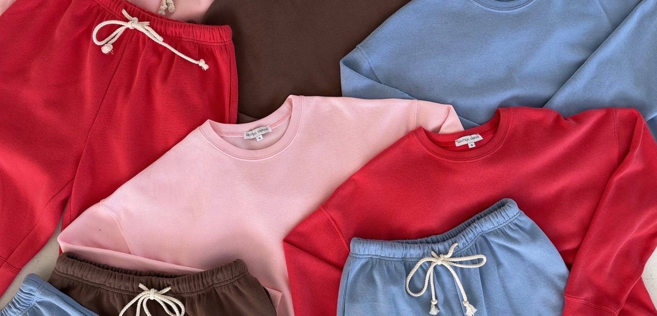 Collection of colorful clothing including sweatshirts and shorts on a neutral background