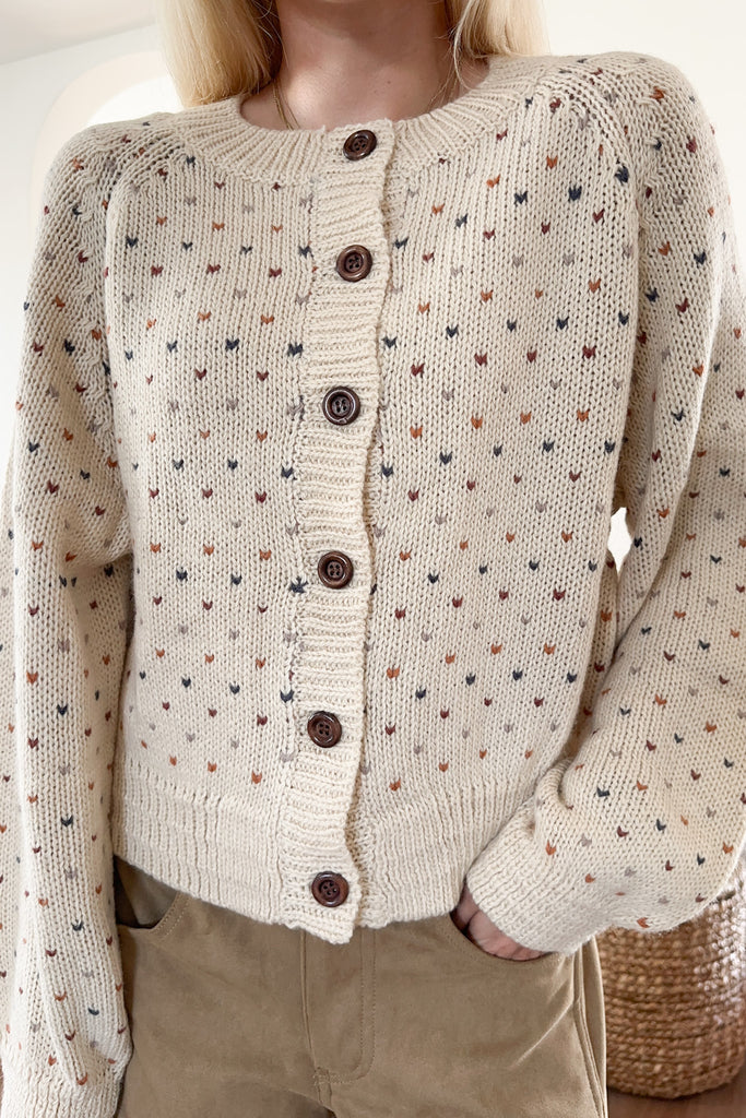 Beige cardigan with button details worn by a person, with a blurred background