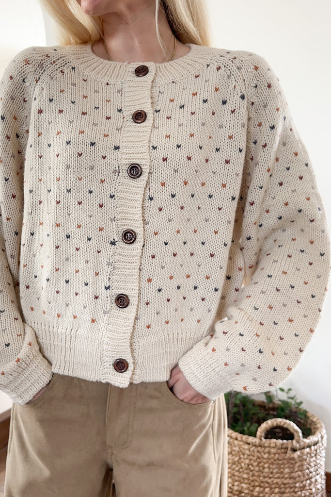 Person wearing a beige knitted cardigan with small patterns and brown buttons.