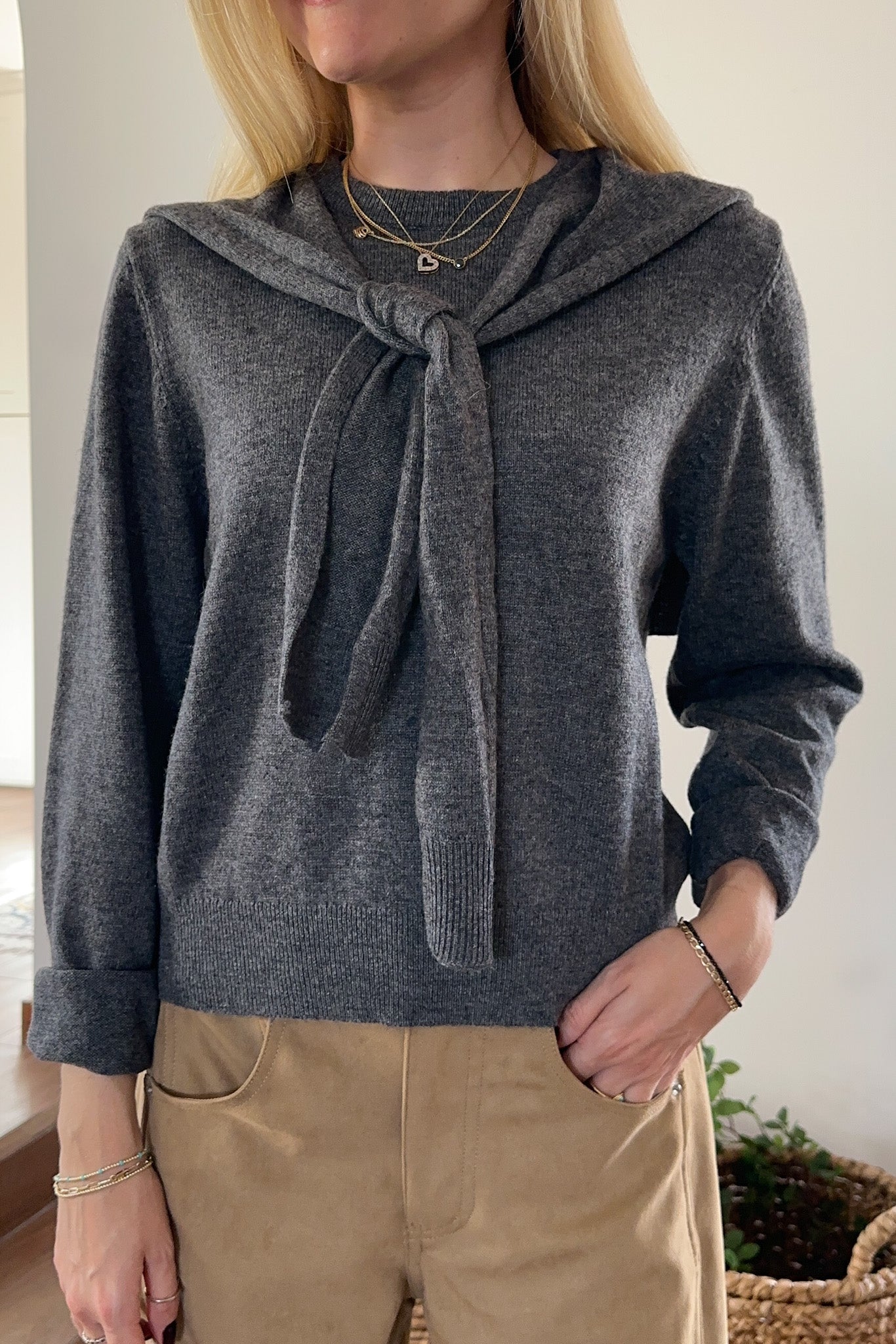 Person wearing a gray sweater with a tie detail, standing indoors.