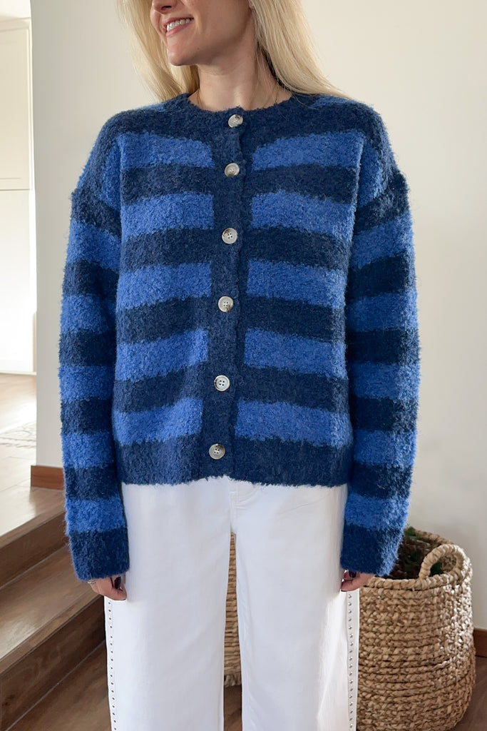Person wearing a blue striped cardigan with white pants indoors.