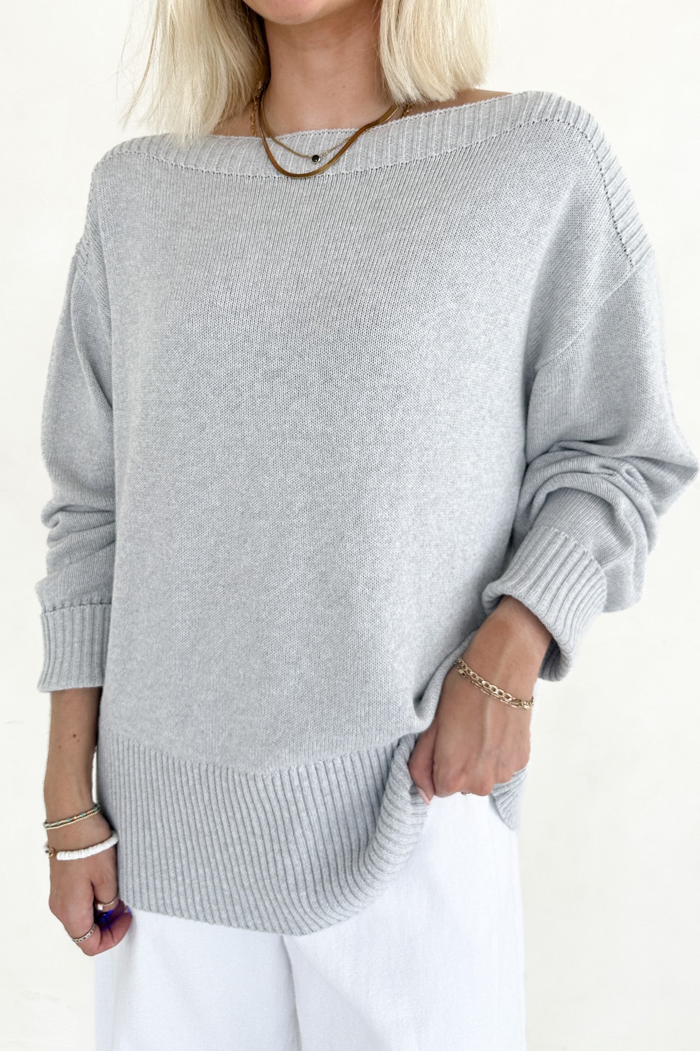 Person wearing a gray sweater and white pants on a plain background