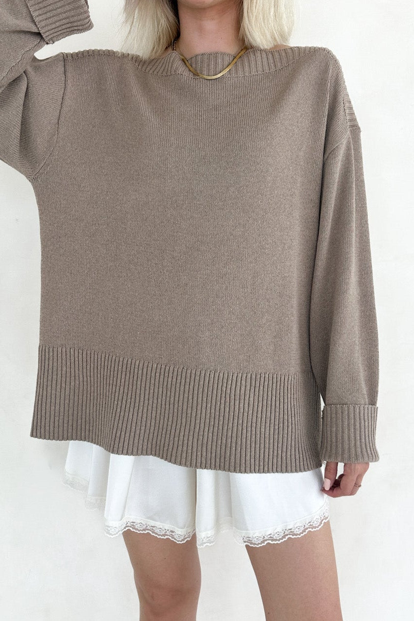 Woman wearing a brown sweater over a white dress on a white background