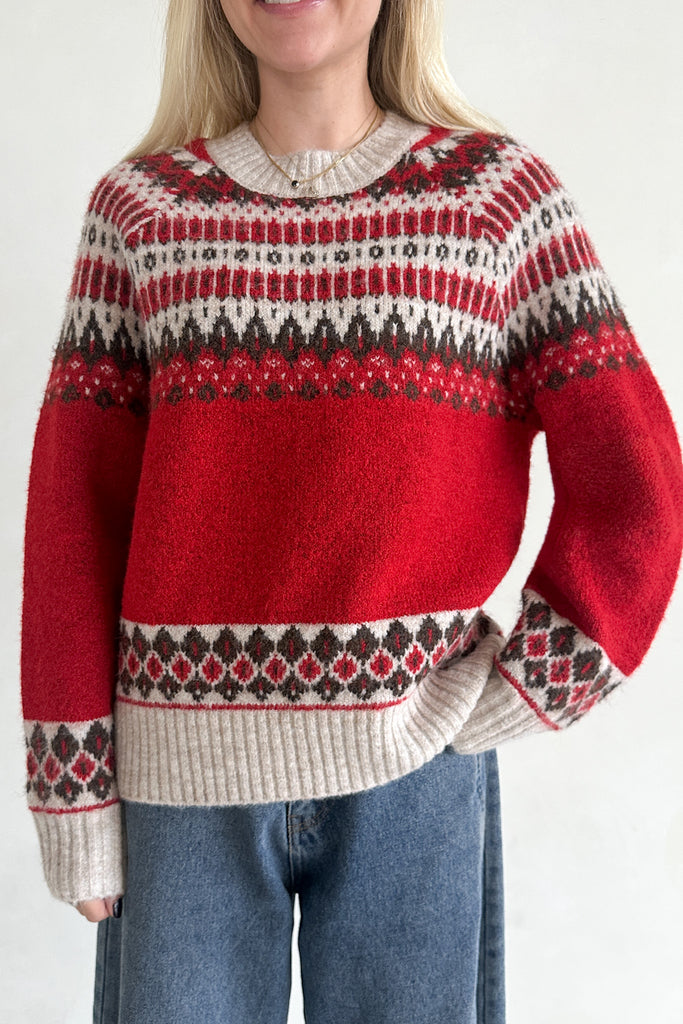 Person wearing a red and patterned sweater with blue jeans on a plain background