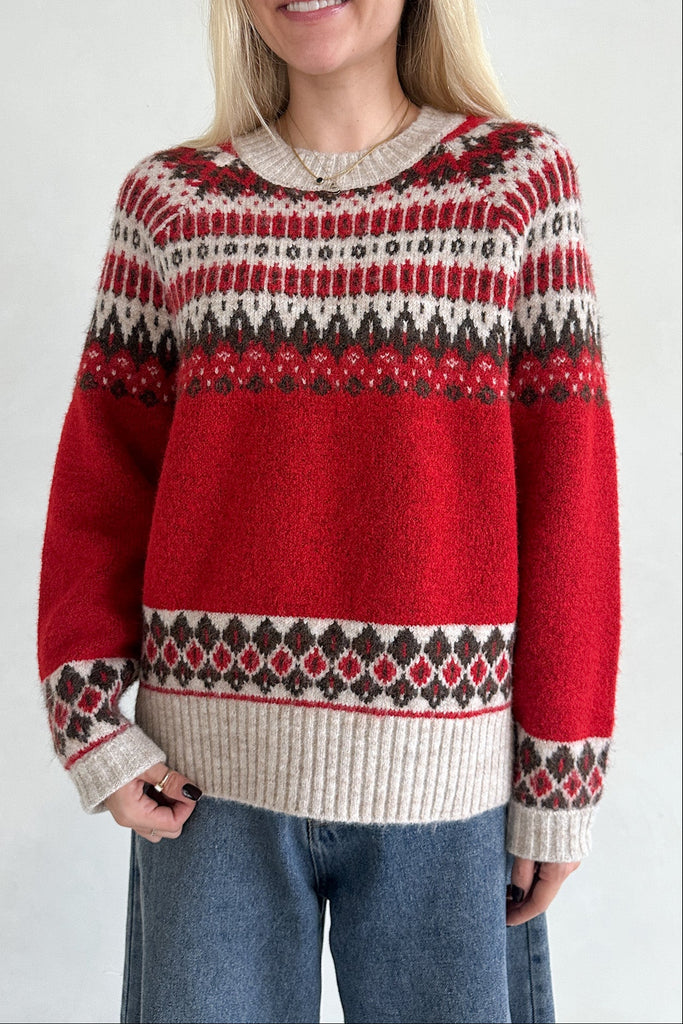 Person wearing a red patterned sweater with blue jeans on a white background