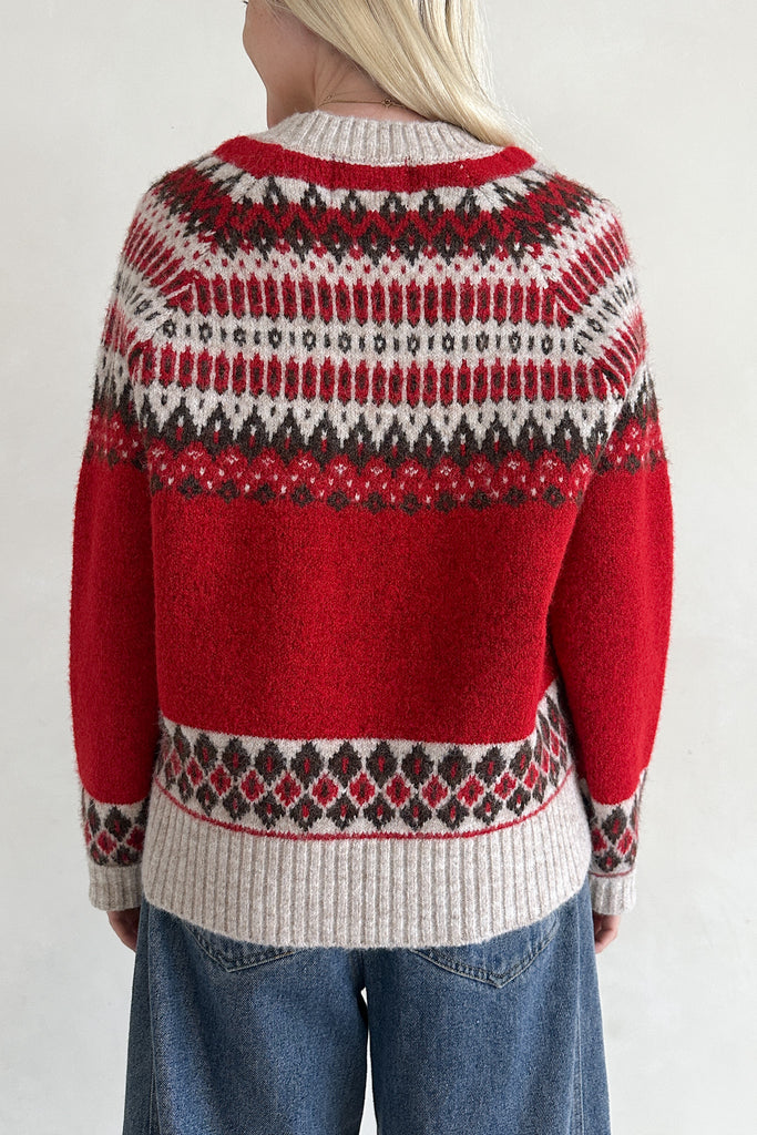 Red and white patterned sweater worn by a person on a plain background