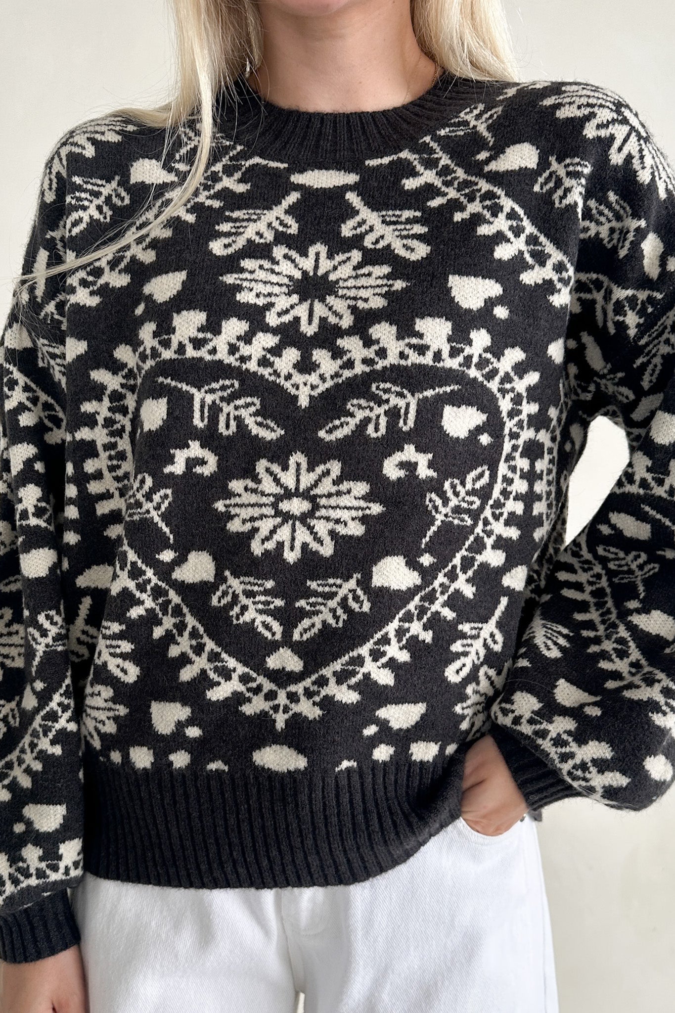 Black sweater with white heart and floral pattern worn by a person