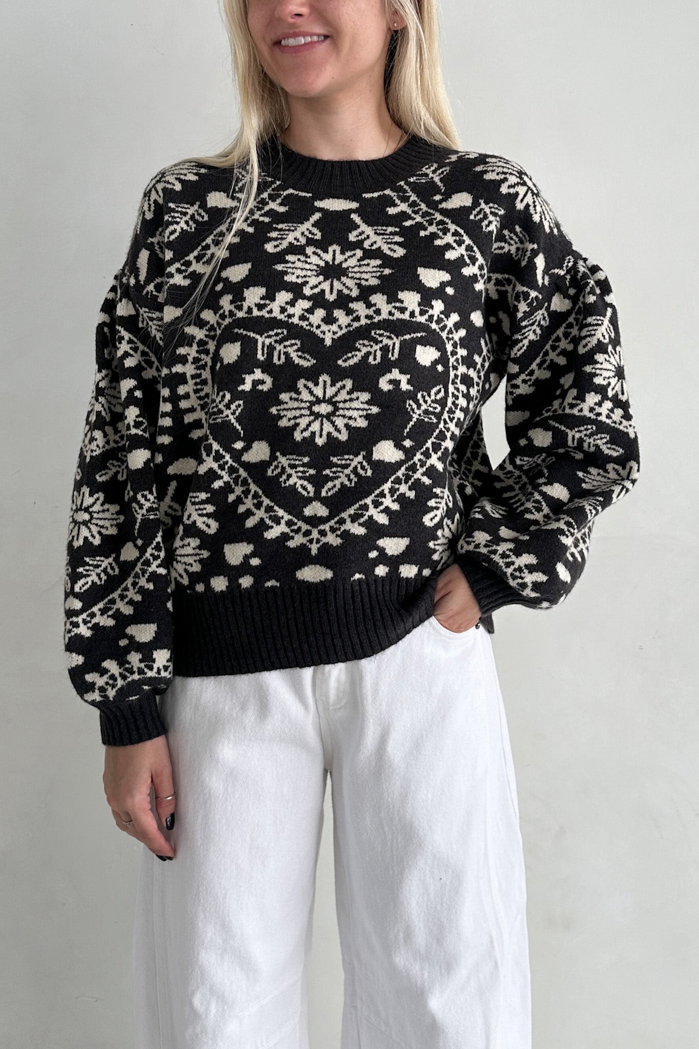 Person wearing a black sweater with white patterns on a plain background
