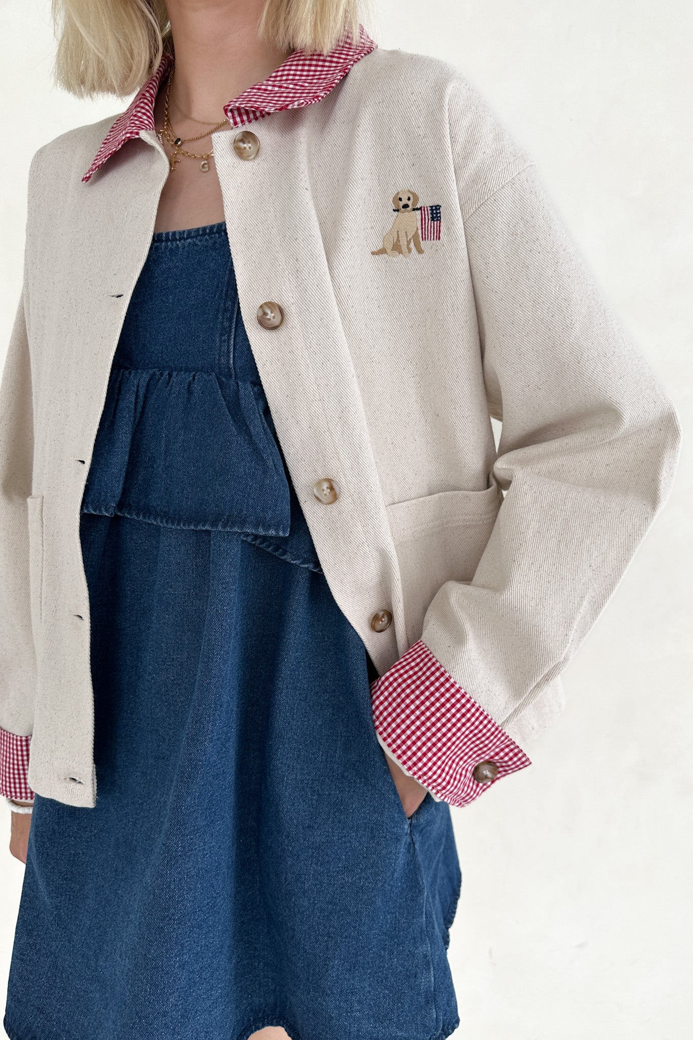 Person wearing a beige jacket with red checkered trim over a blue dress on a white background