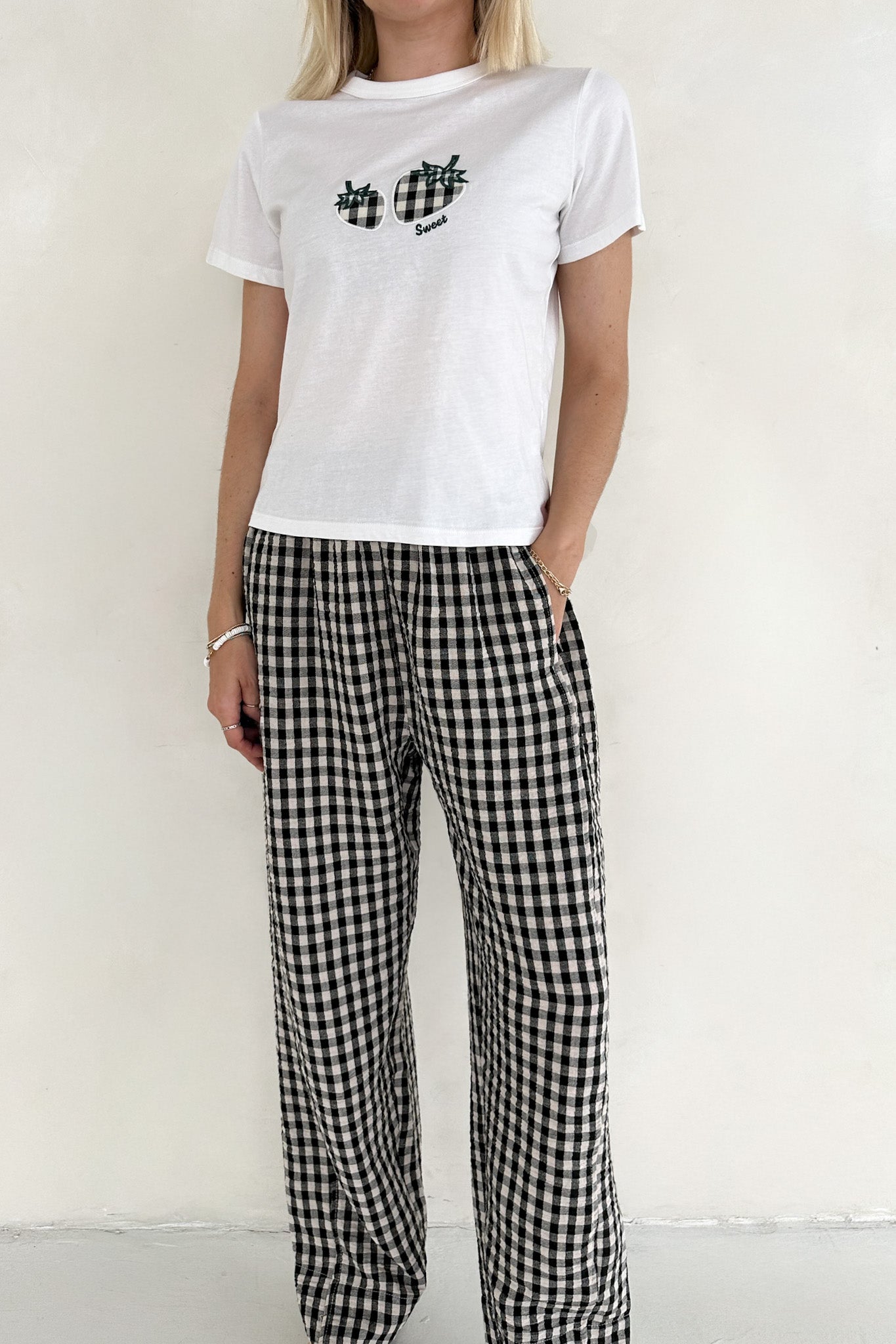 Person wearing a white t-shirt with black text and plaid pants on a plain background