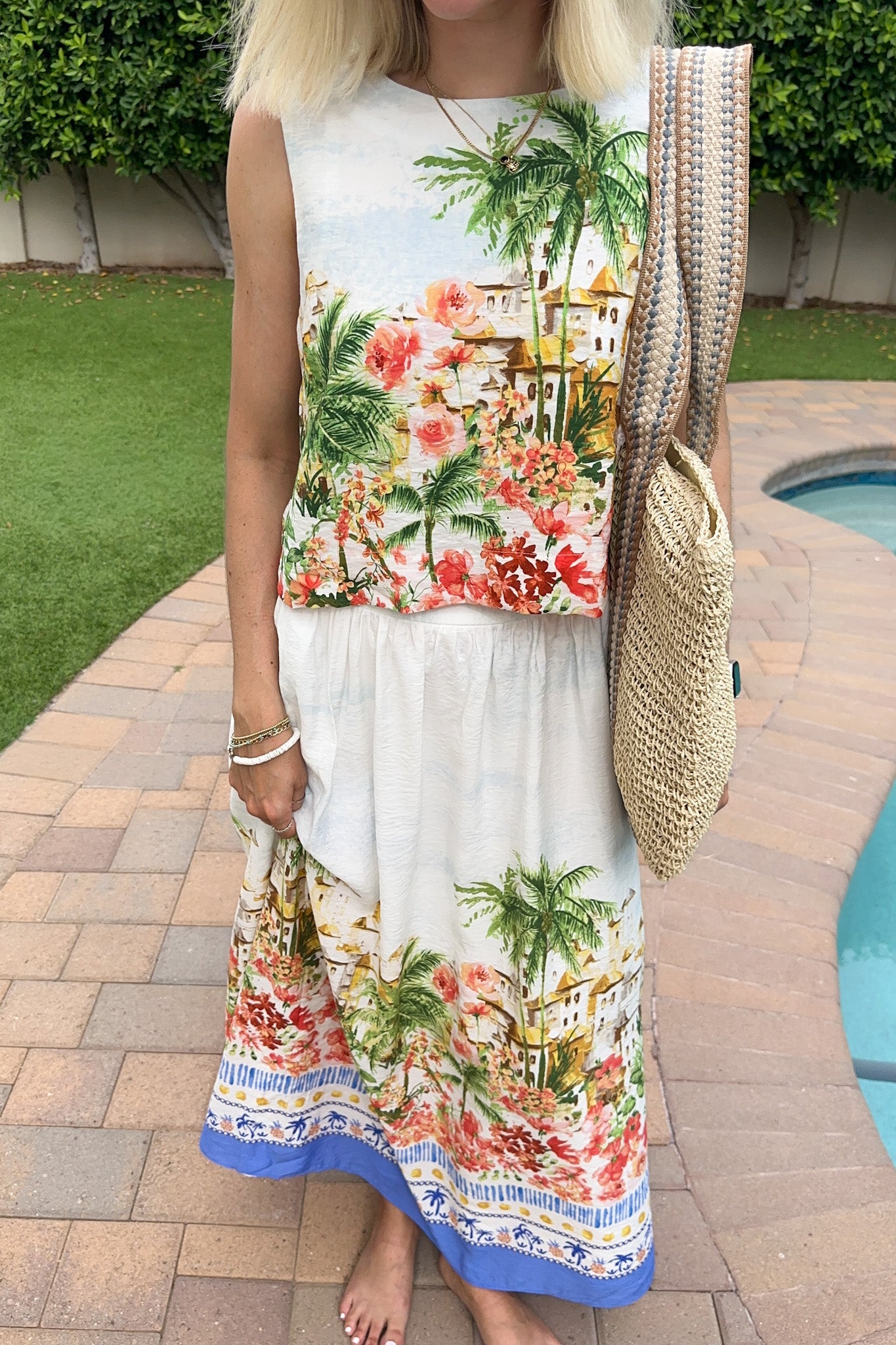 Woman wearing a colorful dress with palm tree and floral design, standing by a pool.
