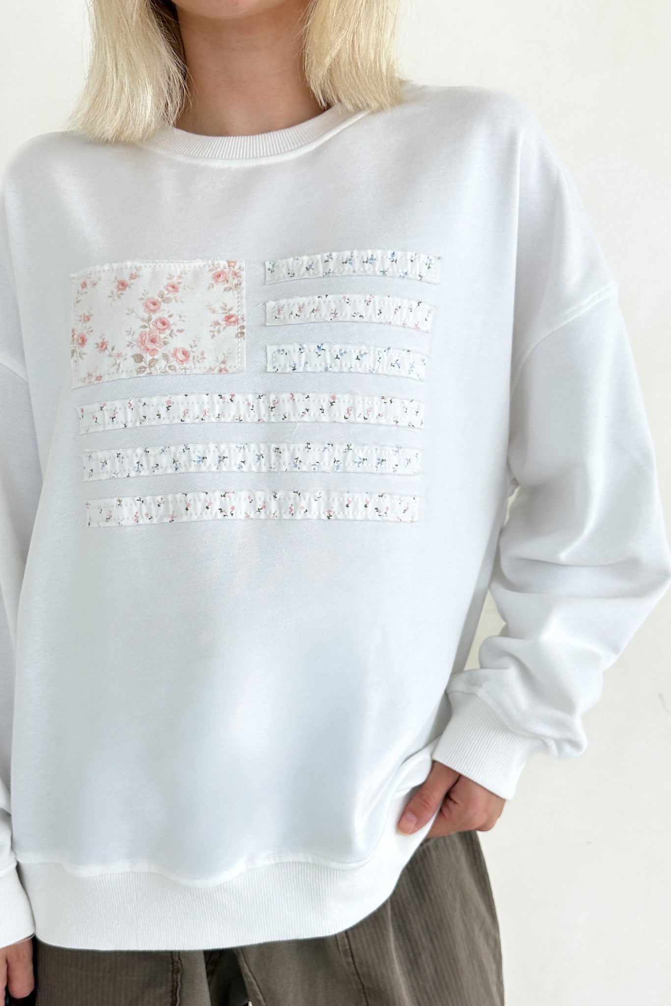 White sweatshirt with lace details and floral design on a plain background