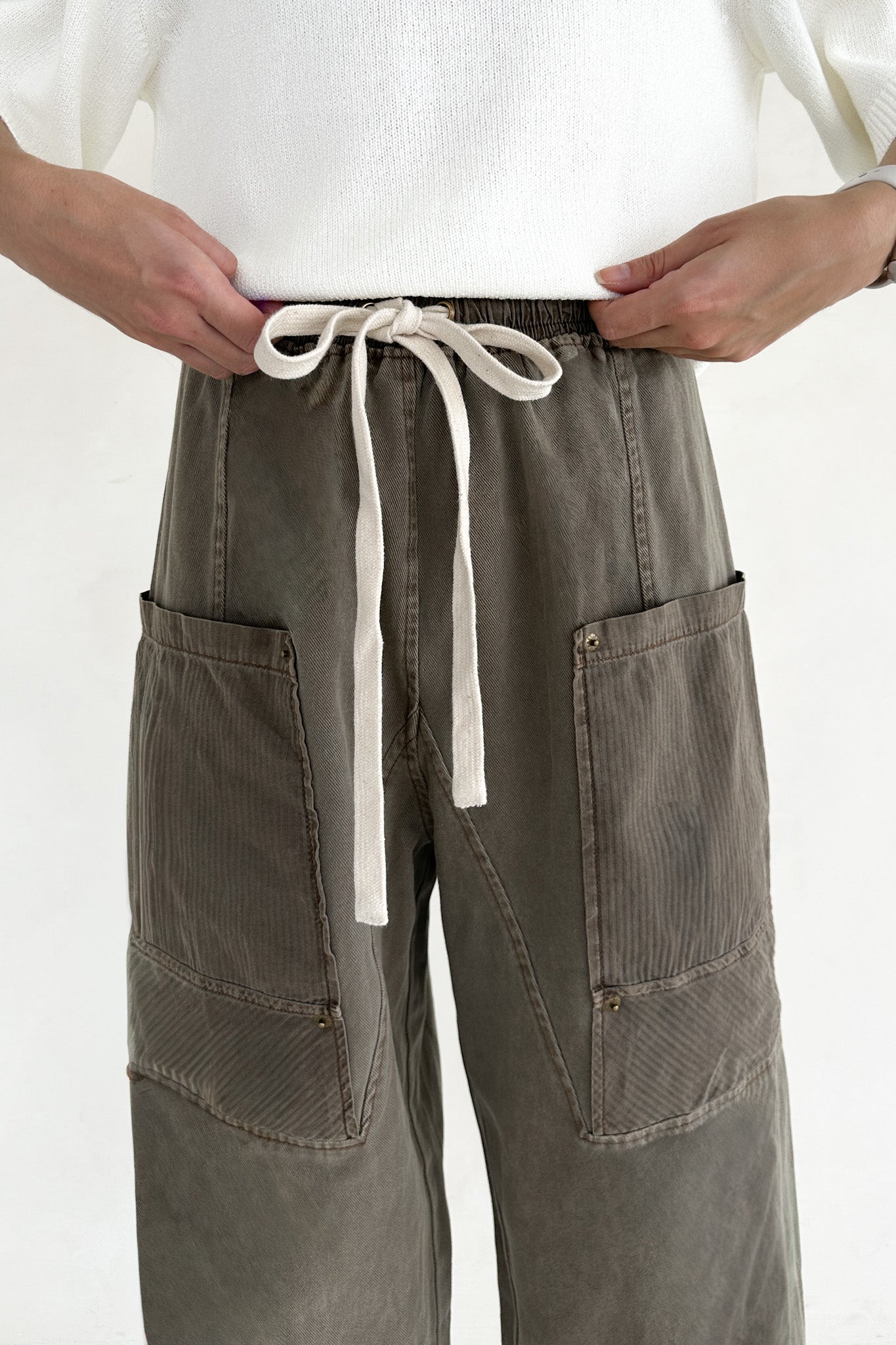 Person wearing brown pants with a white drawstring on a plain background