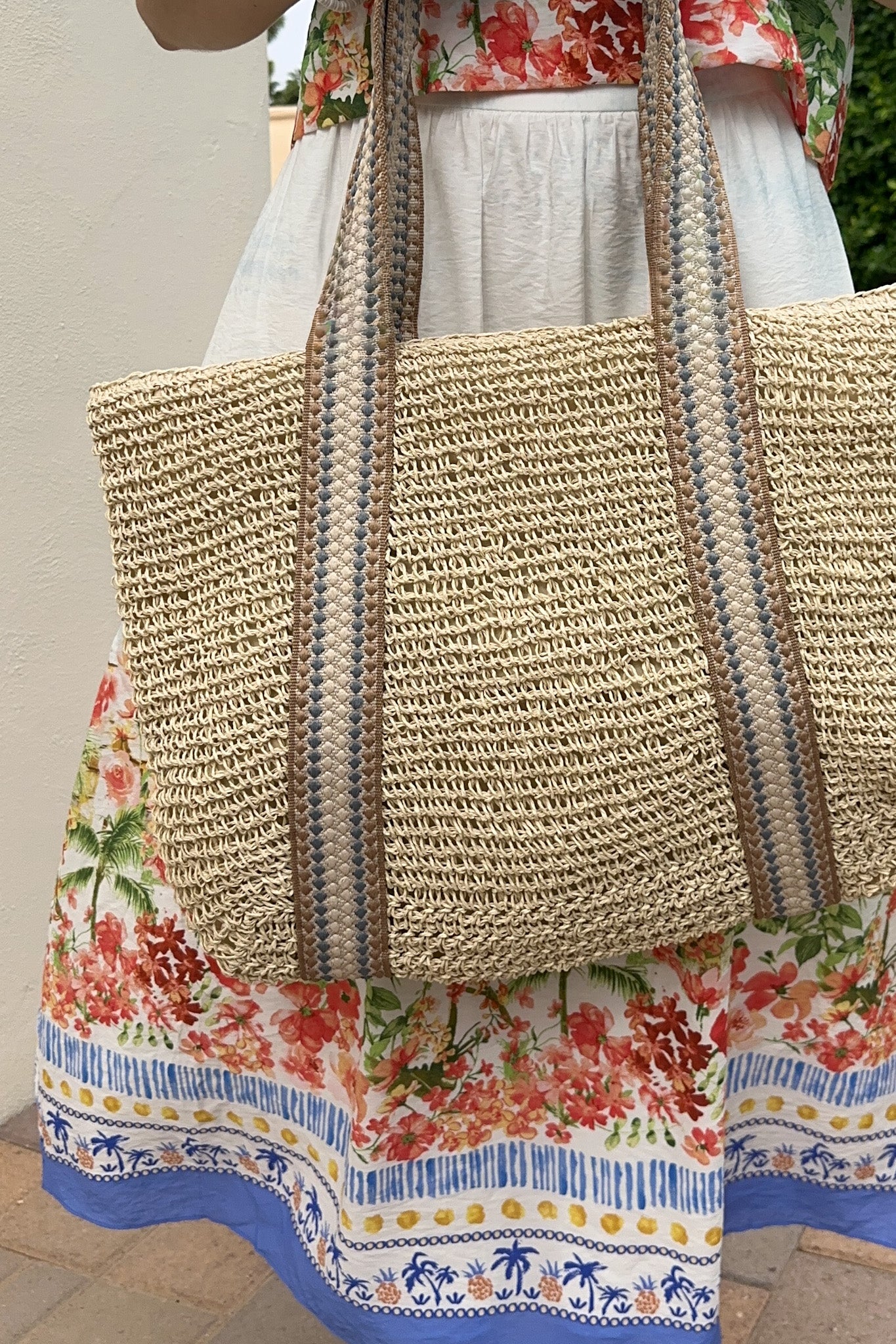 Person wearing a floral dress with a textured straw bag.