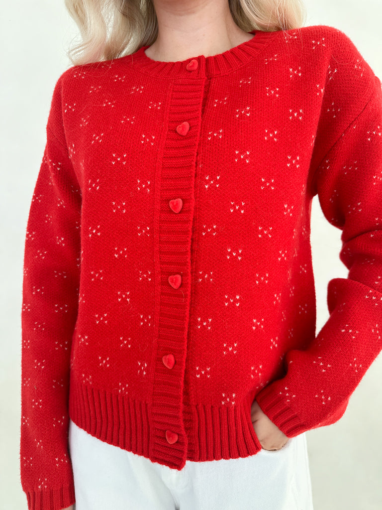 Red knitted cardigan with heart patterns on a white background