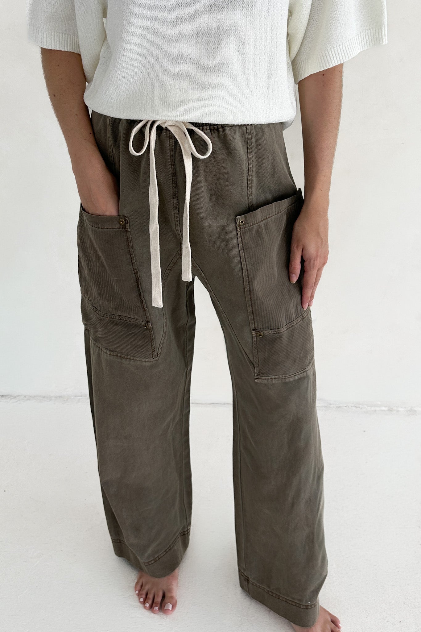 Person wearing olive green cargo pants with a white top on a white background