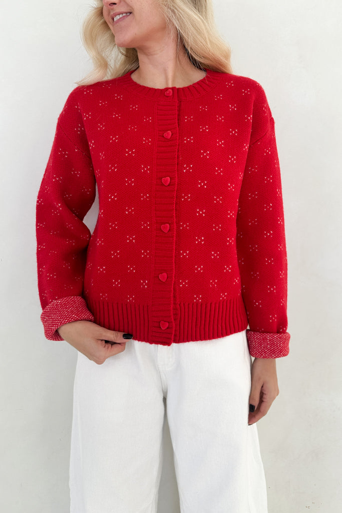 Person wearing a red knitted cardigan with heart patterns on a white background