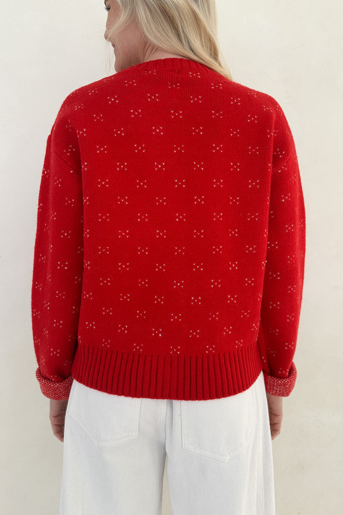Person wearing a red sweater with a subtle pattern on a plain background