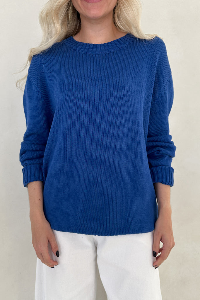 Person wearing a blue sweater and white pants against a plain background