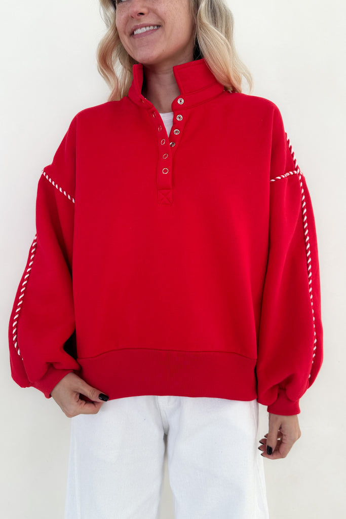 Person wearing a red sweater with white trim on a plain background
