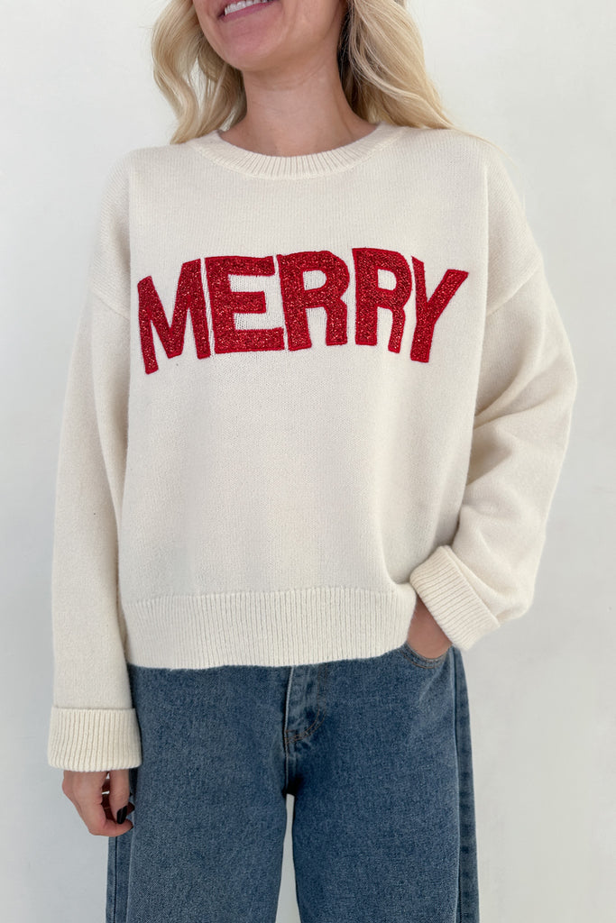 Person wearing a cream sweater with 'MERRY' in red text on a plain background