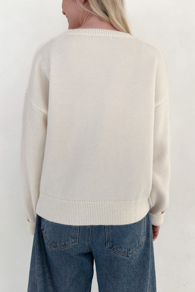 Person wearing a cream sweater and blue jeans on a white background
