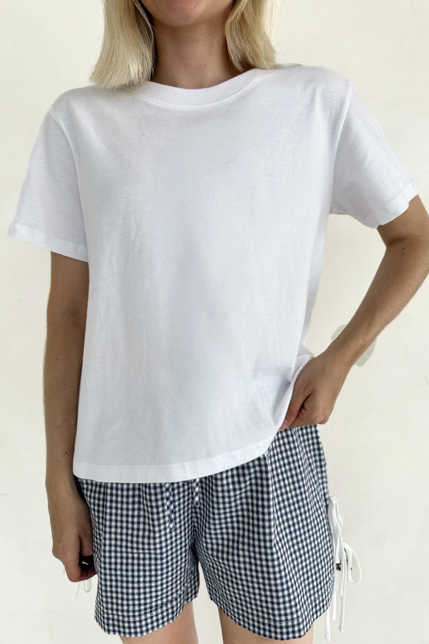 Person wearing a white t-shirt and checkered shorts on a plain background
