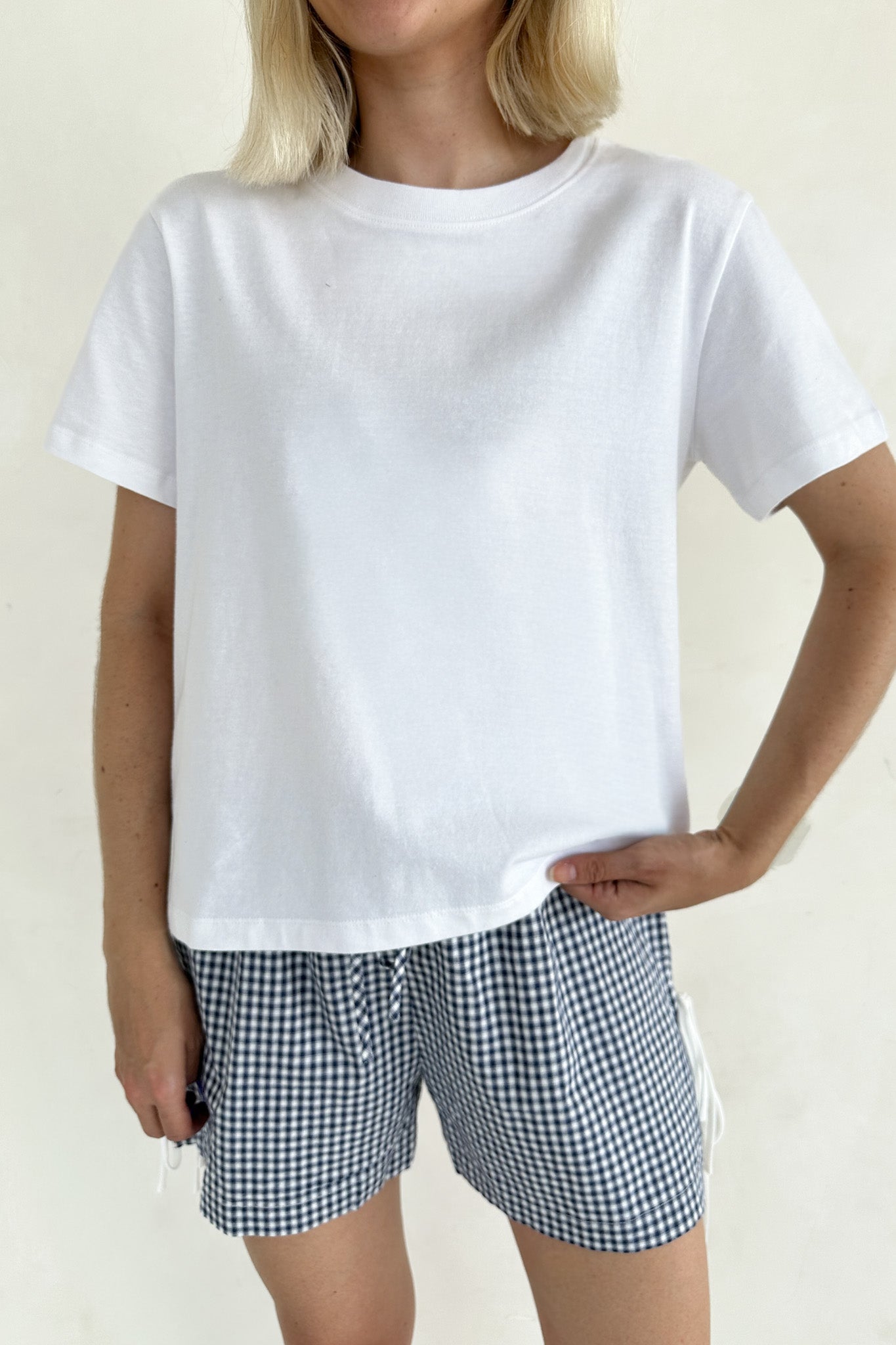 Person wearing a white t-shirt and checkered shorts on a plain background