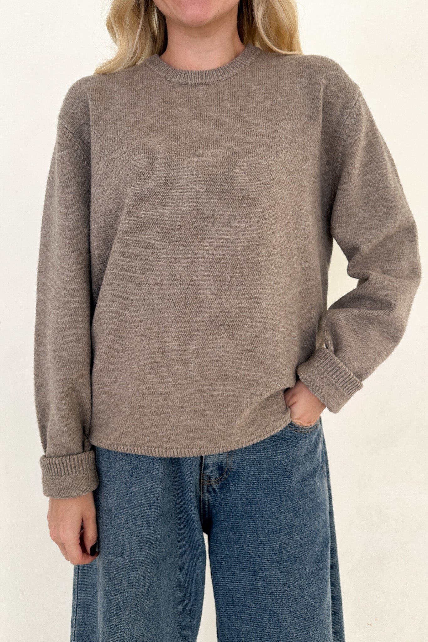 Person wearing a brown sweater and blue jeans on a white background