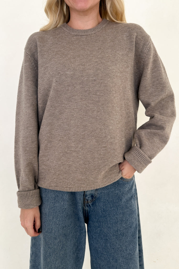 Person wearing a brown sweater and blue jeans on a white background
