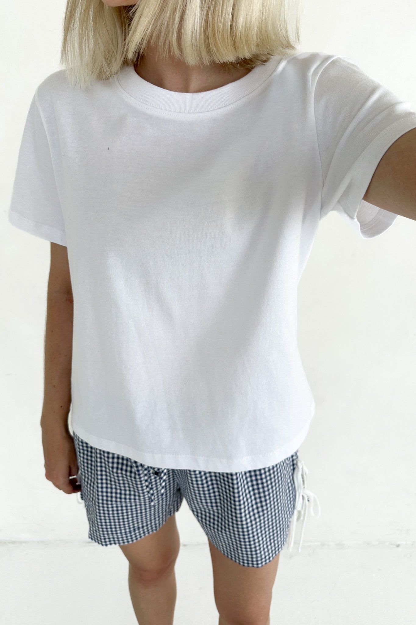 Person wearing a plain white t-shirt and checkered shorts on a light background