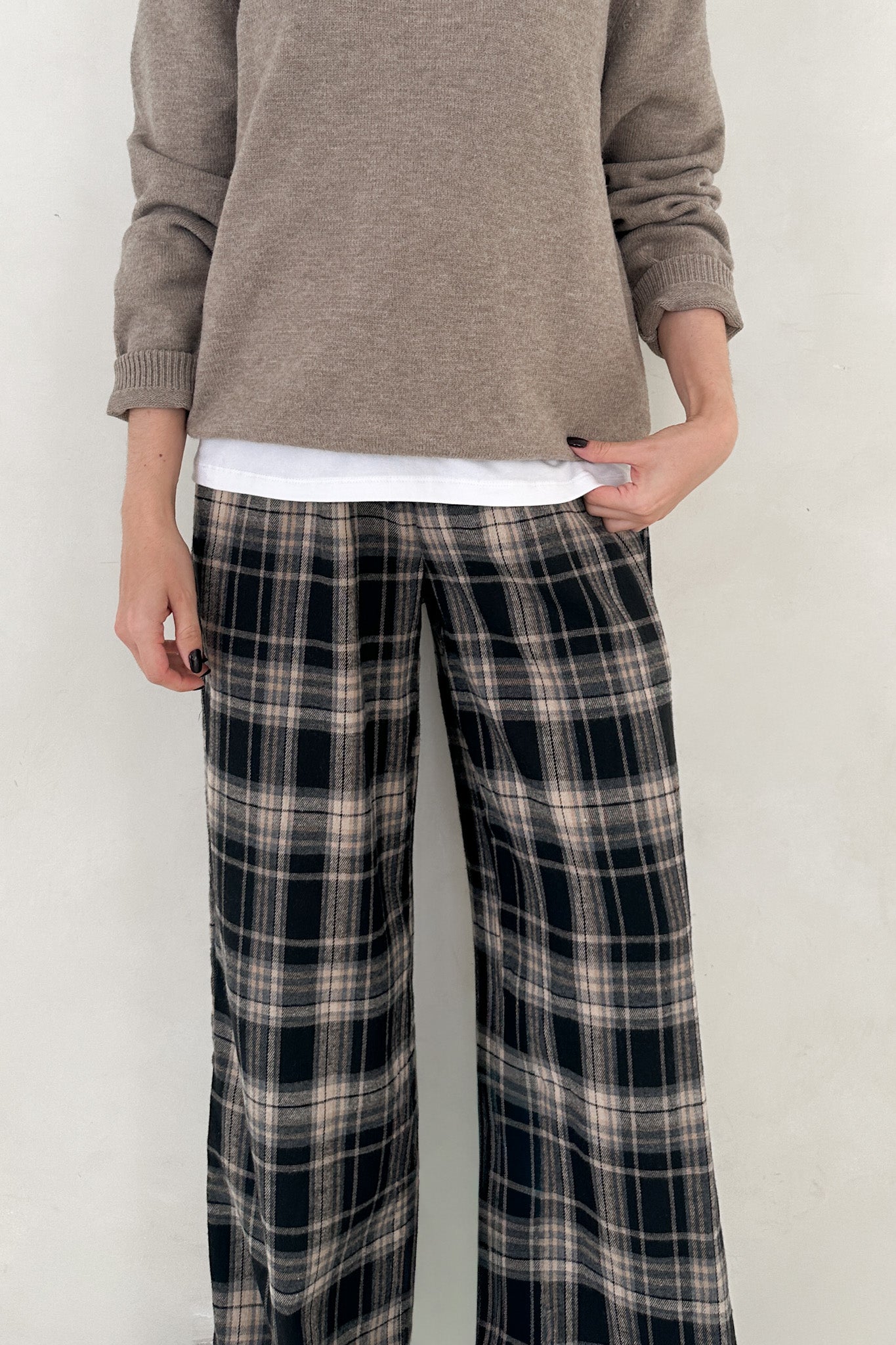 Person wearing plaid pants and a brown sweater against a white background