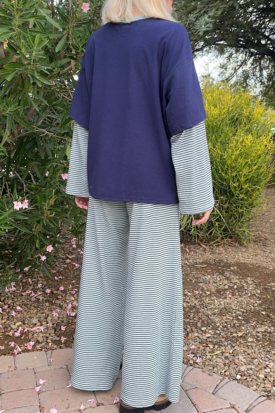A woman stands outdoors in a garden wearing a loose navy top with striped long sleeves and matching wide-leg striped pants.