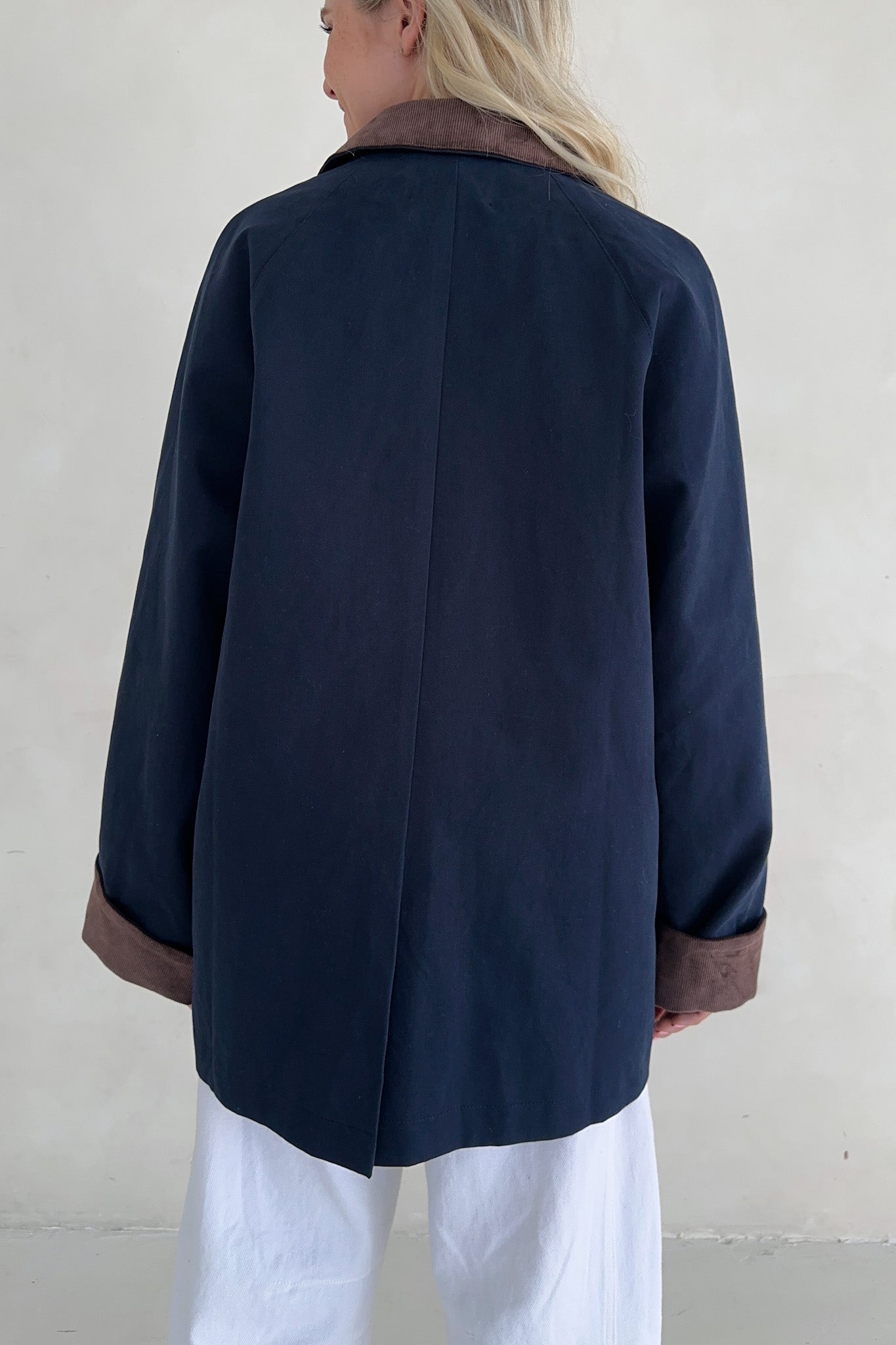 Person wearing a navy blue coat with brown trim on a plain background