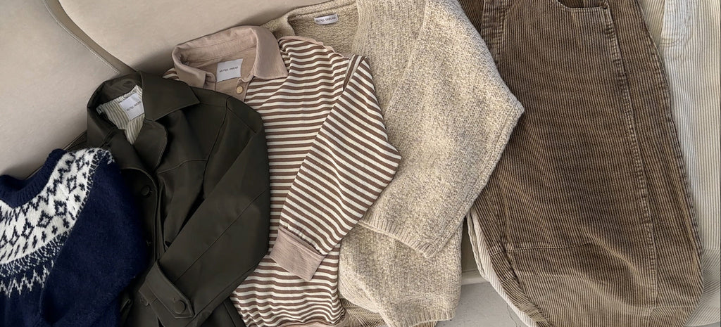 Stack of folded clothes including a sweater, pants, and shirts on a beige surface.