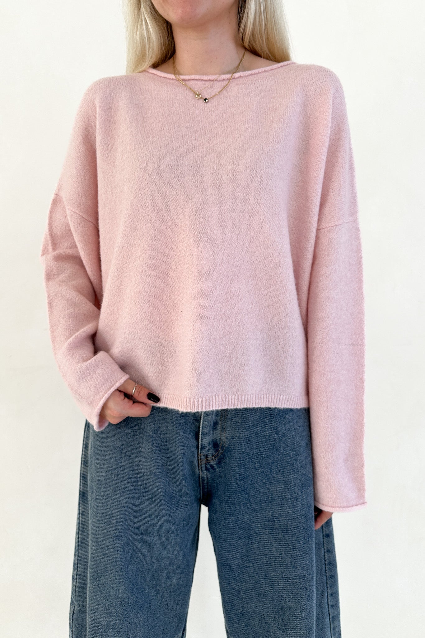 Person wearing a pink sweater and blue jeans on a plain background