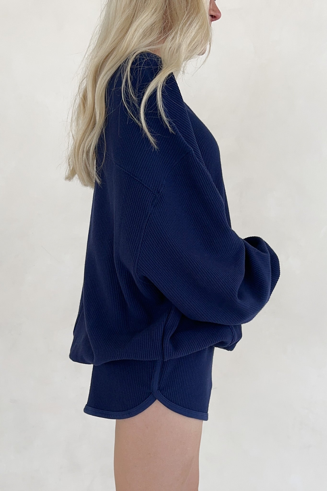 Person wearing a navy blue sweater and shorts set on a white background