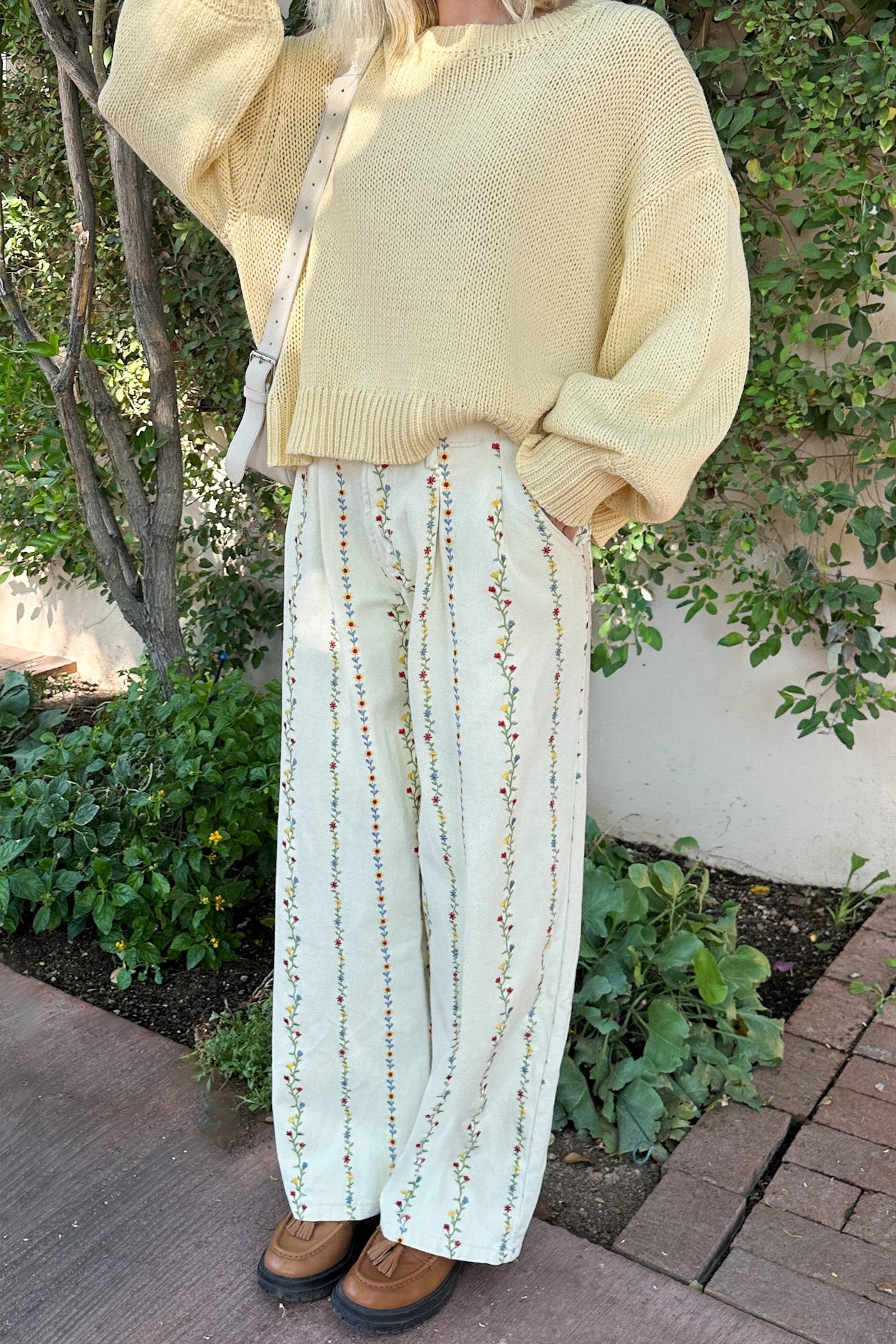 Person wearing a light yellow sweater and patterned pants standing outdoors.