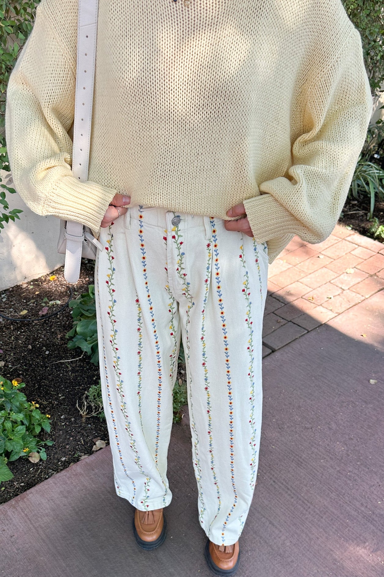 Person wearing a light yellow sweater and white pants with small patterns outdoors.