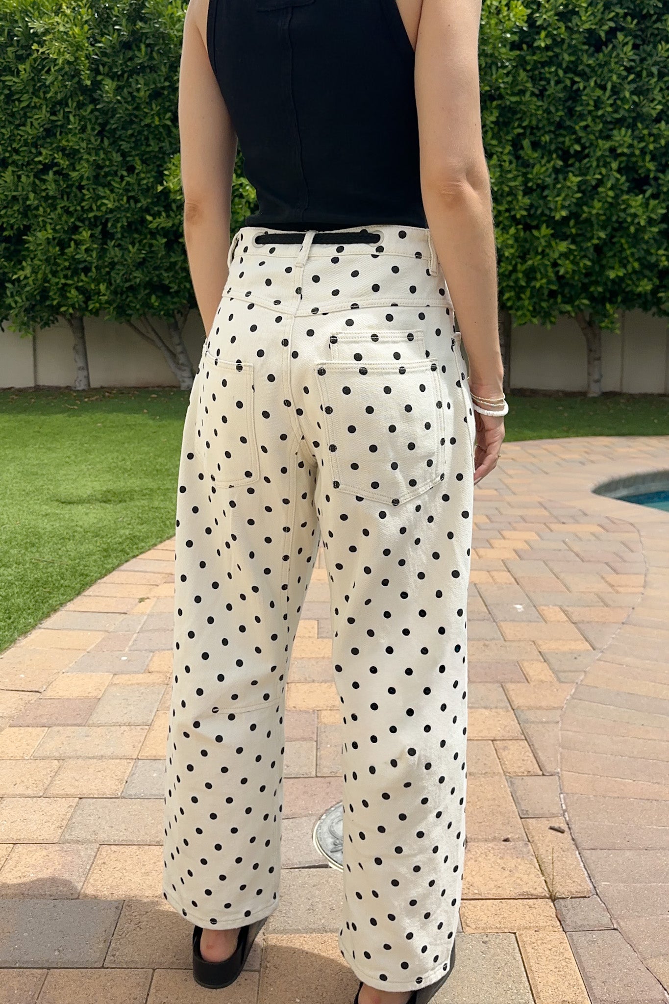 Person wearing black polka dot pants standing on a patio with greenery in the background
