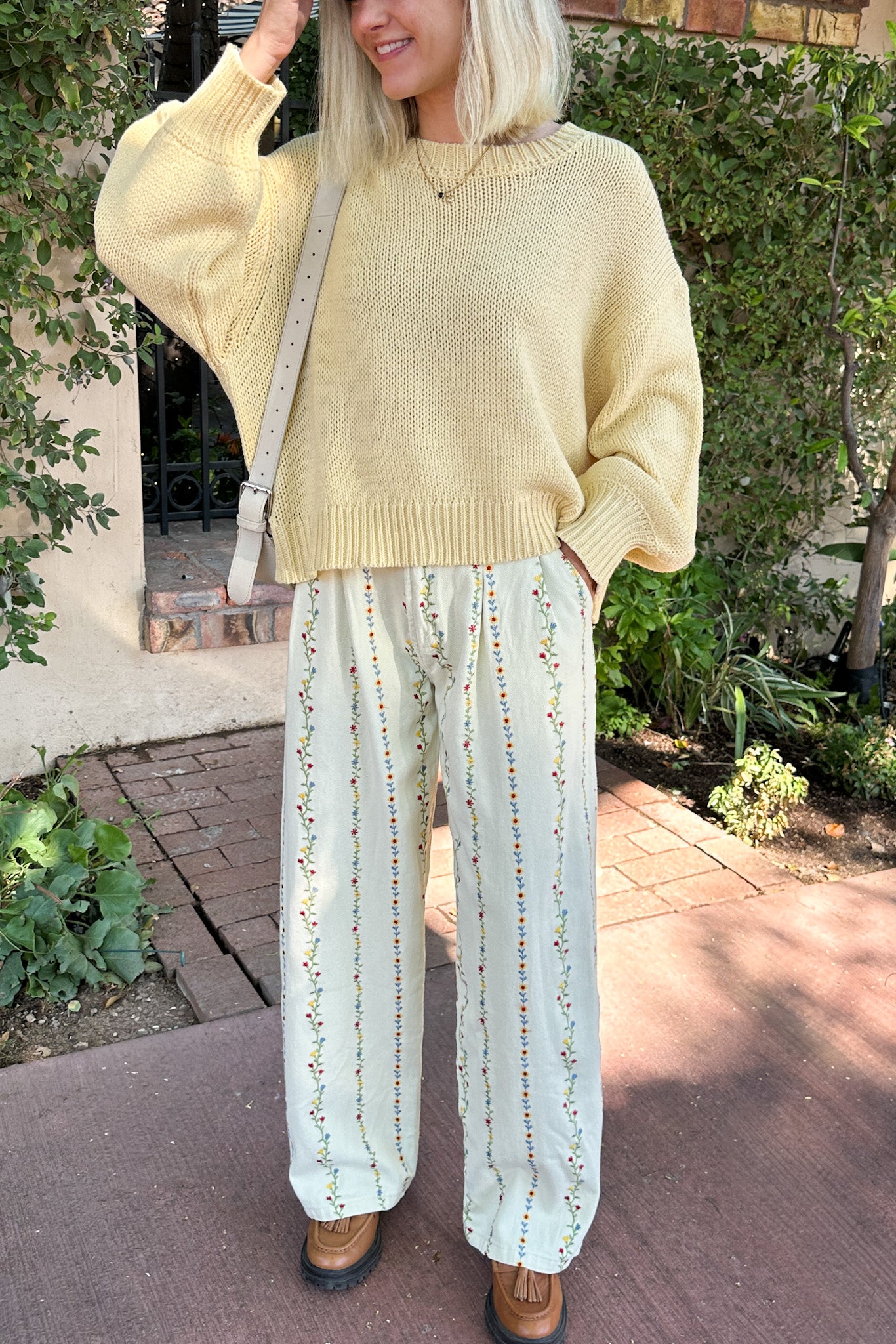 Person wearing a yellow sweater and light-colored pants standing outdoors.