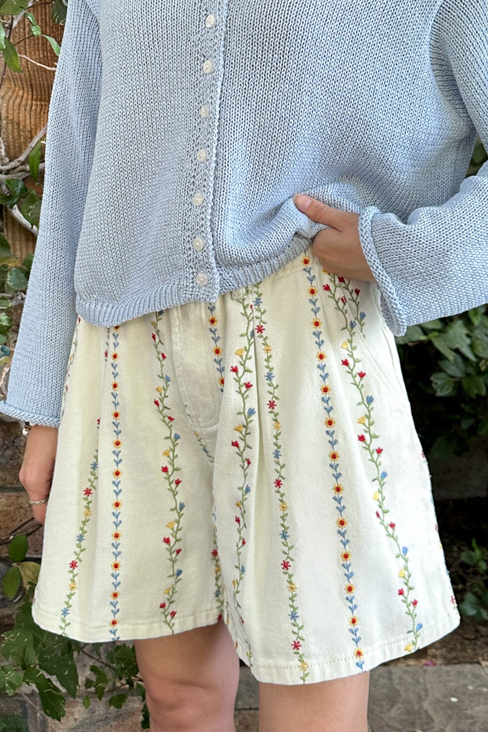Person wearing a light blue cardigan over a patterned skirt with a natural background