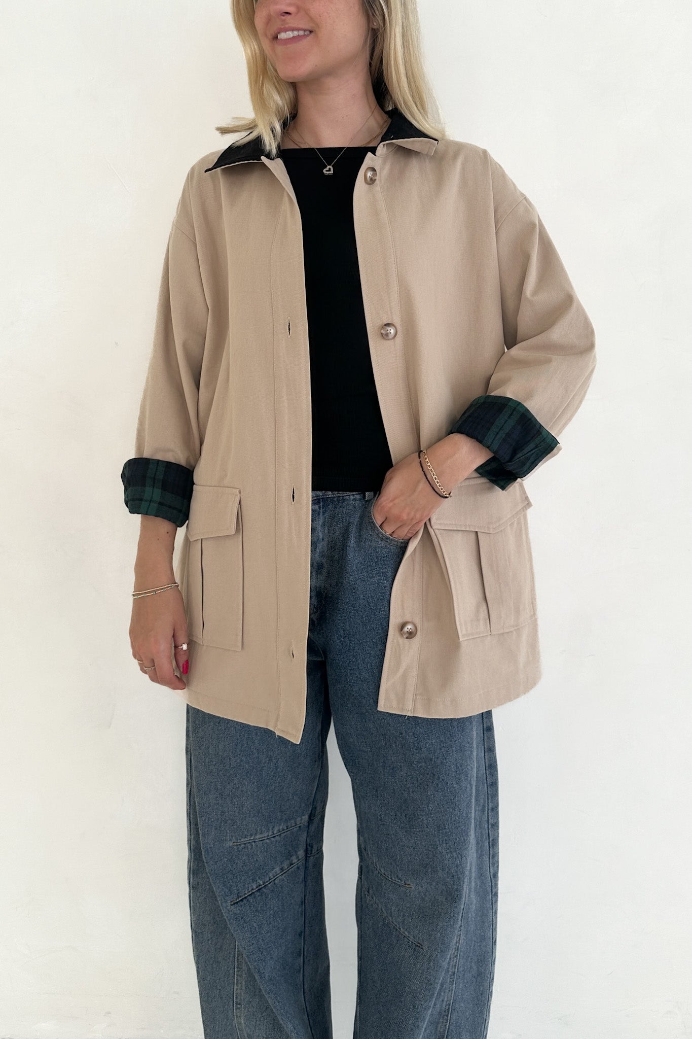 Person wearing a beige jacket with black cuffs and collar on a white background